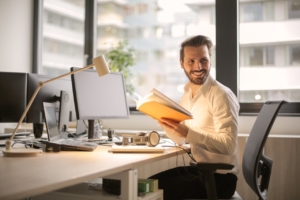 A man at a office desk holding a book